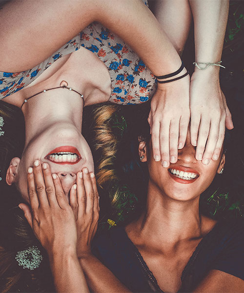 zwei Frauen liegend, halten sich gegenseitig die Augen zu, lachend