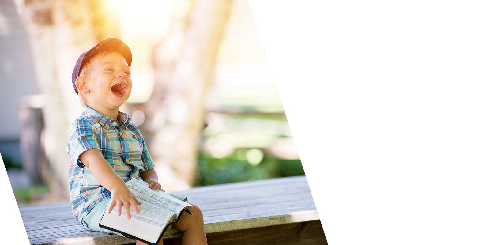 kleiner Junge mit Mütze und Buch lachend